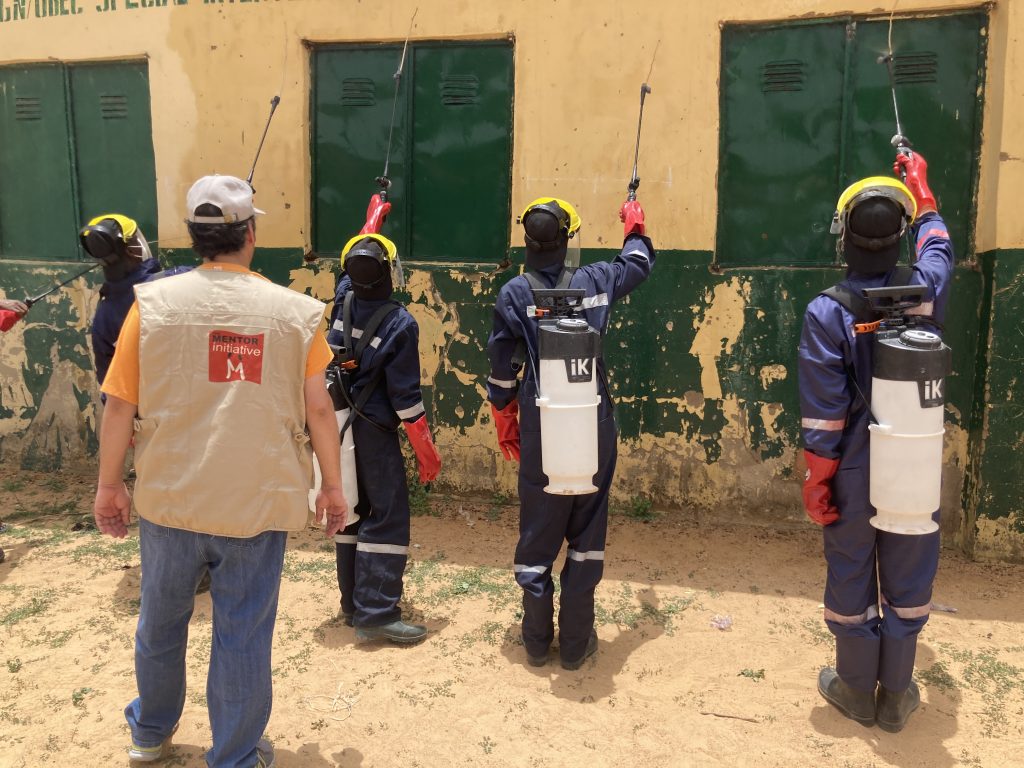 MENTOR officer watching three people spray a wall with insecticide